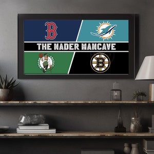 May include: A framed print with a black background and the text "The Nader Mancave" in white. The print is divided into four sections, each featuring a different sports team logo: the Boston Red Sox, the Boston Celtics, the Miami Dolphins, and the Boston Bruins.