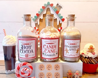 May include: Three glass jars with cork tops and red and white checkered labels. The labels read "Mrs. Claus", "Hot Cocoa", "Candy Cane Crunch", and "Gingerbread Spice". The jars are arranged on a wooden shelf with a gingerbread house behind them. There are also cookies, a candy cane, and a gingerbread man cupcake.
