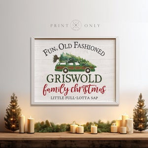 Puede incluir: Un letrero de madera blanca con una camioneta verde que lleva un &aacute;rbol de Navidad. El letrero dice "Fun, Old Fashioned Griswold Family Christmas, Little Full, Lotta Sap".