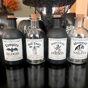 May include: Four black glass bottles with cork stoppers and labels. The labels have black and white illustrations of a bat, a ghost, a dragon, and a werewolf. The labels also have text that reads "Vampire Blood", "Doll Tears", "Dragon's Breath Potion", and "Werewolf Saliva".