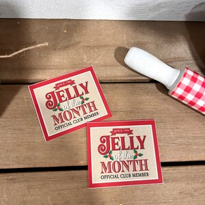 May include: Two red and brown square stickers with the text "JELLY of the MONTH" and "OFFICIAL CLUB MEMBER" on a wooden surface.