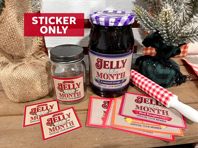 May include: A set of five "Jelly of the Month" stickers featuring different fruit flavors: Concord Grape, Red Raspberry, Orange Marmalade, and two others. The stickers are printed on a brown background with red and white lettering. The stickers are displayed on a wooden surface with a jar of jelly, a burlap sack, and a red and white checkered rolling pin.