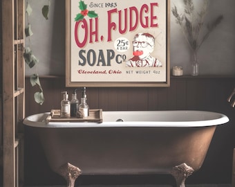 May include: A square framed wall sign featuring the text "OH, FUDGE SOAP CO." in red and dark gray, with "SINCE 1983", "25¢ A BAR", "CLEVELAND, OHIO", and "NET WEIGHT 4oz". It includes a graphic of a child with glasses and holly leaves.
