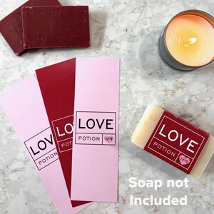 May include: Three pink and red rectangular labels with the text "LOVE POTION No.9" printed in black. The labels are stacked on top of each other. A small white bar of soap with the same text is shown in the bottom right corner. The text "Soap not included" is printed below the soap.