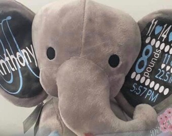 Op de afbeelding: Een grijze pluche olifant met zwarte oren. De oren zijn versierd met blauwe en witte tekst. Het ene oor zegt "Anthony" en het andere oor zegt "11-14-2010 8 pounds 11 oz. 22.5 in. 5:57 PM".