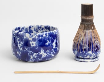 Op de afbeelding: Een blauwe en witte keramische matcha-kom met een bamboe garde en een bamboe matcha-lepel. De kom heeft een gespikkelde blauwe en witte glazuur.