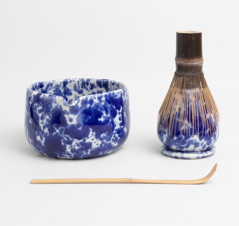 K&ouml;nnte beinhalten: Eine blaue und wei&szlig;e Keramik-Matcha-Schale mit einem Bambus-Schneebesen und einem Bambus-Matcha-L&ouml;ffel. Die Schale hat eine gesprenkelte blaue und wei&szlig;e Glasur.