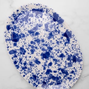 Puede incluir: Plato ovalado para servir con base blanca y diseño de salpicaduras azules. El plato de cerámica tiene una superficie lisa y es ideal para servir aperitivos o postres. La pintura azul se aplica en varios tamaños, creando un patrón único.