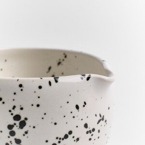 Puede incluir: Taz&oacute;n de cer&aacute;mica blanco con un dise&ntilde;o moteado en blanco y negro. El taz&oacute;n tiene una forma redondeada y un borde ligeramente acampanado.