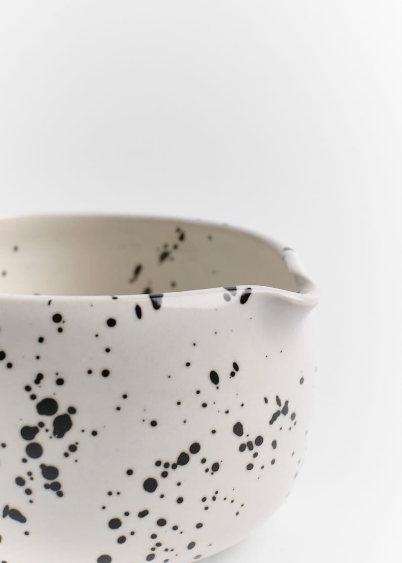 Puede incluir: Taz&oacute;n de cer&aacute;mica blanco con un dise&ntilde;o moteado en blanco y negro. El taz&oacute;n tiene una forma redondeada y un borde ligeramente acampanado.