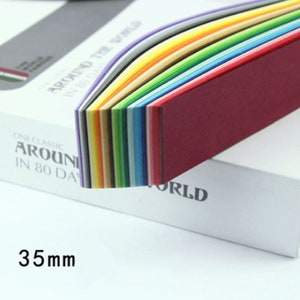 May include: A stack of colorful paper sheets in a rainbow pattern. The paper is 35mm wide and is part of a set called "One Classic Around the World in 80 Days".