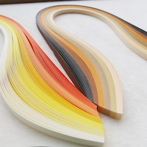 May include: A set of paper quilling strips in a range of warm colours, including white, yellow, orange, brown, and black. The strips are arranged in a curved shape, creating a visually appealing pattern.