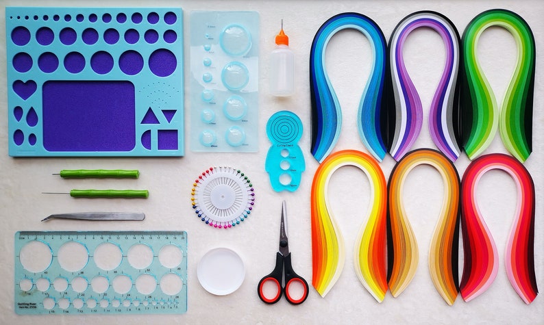 May include: A set of paper quilling tools and supplies, including a variety of coloured paper strips, a quilling tool, a ruler, a circle template, a pincushion, a bottle of glue, and a pair of scissors.