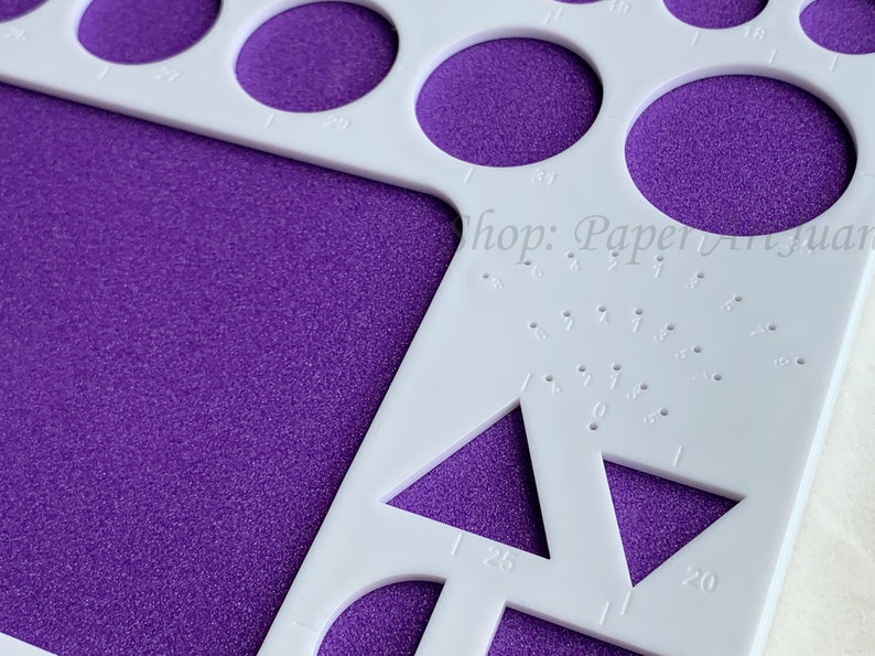 May include: White plastic circle and triangle template with various sizes marked in inches. The template is on a purple textured surface. The text "Shop: Paperyuan" is visible in the upper right corner.