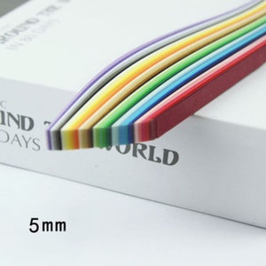 May include: A pack of 5 mm wide, rainbow colored paper strips. The strips are arranged in a rainbow pattern, with the red strip on the bottom and the purple strip on the top. The strips are curved slightly, giving them a wave-like appearance. The text "WORLD" is visible on the white surface the strips are resting on.