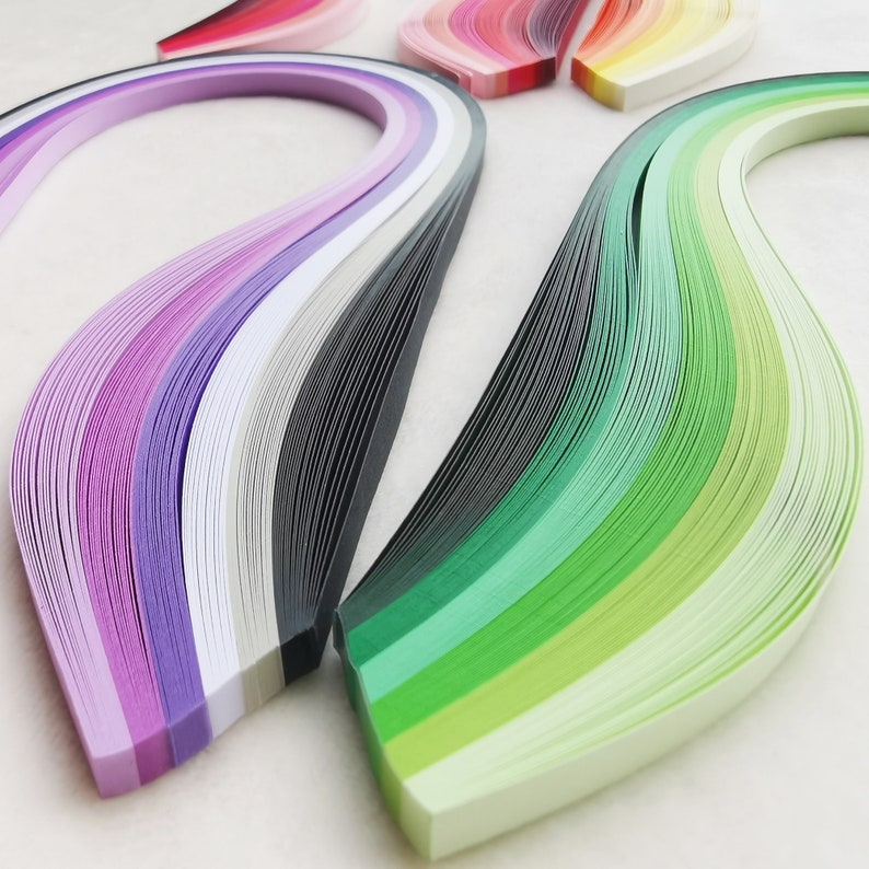 May include: A set of colourful paper strips, arranged in a wave pattern. The strips are in shades of purple, grey, white, green, and light green.