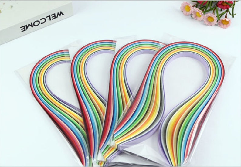 May include: A pack of rainbow colored paper strips for crafting. The strips are arranged in a rainbow pattern and are packaged in clear plastic.