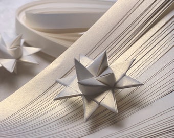 Puede incluir: Primer plano de una estrella de origami blanca, hecha con tiras de papel, sobre un fondo de tiras de papel blancas.