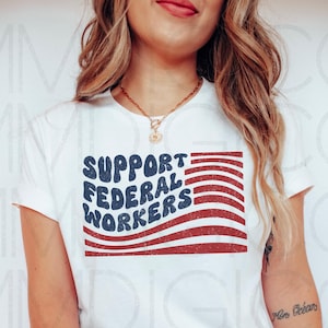 May include: White t-shirt featuring the text "SUPPORT FEDERAL WORKERS" in blue, with a red and white flag design. The shirt has a crew neck.