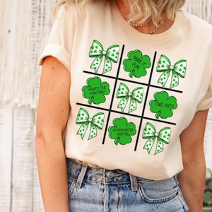 May include: A natural colored t-shirt with a green shamrock and white bow design. The design features the text "Make it Fun", "What's the Function?", "Take Data", and "Session Notes Matter".