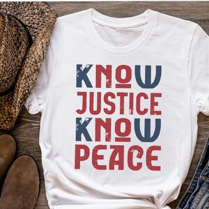 May include: White t-shirt with the text "KNOW JUSTICE KNOW PEACE" in red and blue lettering with a distressed look.