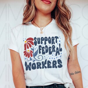 May include: White t-shirt with a red, white, and blue floral design and the text "SUPPORT FEDERAL WORKERS" in blue.