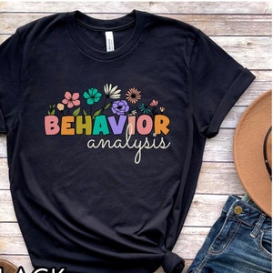 May include: Black t-shirt with a floral design and the text "BEHAVIOR analysis" in rainbow colours.