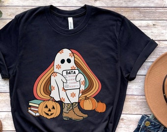 May include: Black t-shirt with a retro-style graphic of a ghost holding a clipboard with the word "DATA" on it. The ghost is wearing cowboy boots and is surrounded by pumpkins and books.