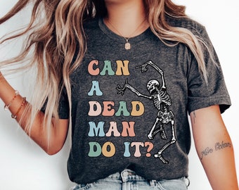 May include: Dark heather grey t-shirt with a skeleton dancing and the text "Can a dead man do it?" in colorful retro font.
