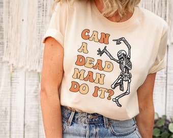 May include: A natural colored t-shirt with a skeleton dancing and the text "Can a dead man do it?" in orange and brown lettering.