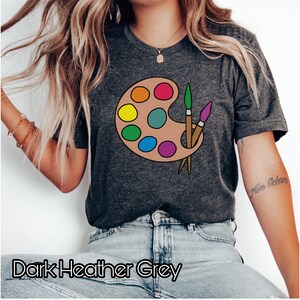 May include: Dark heather grey t-shirt with a colorful paint palette and paintbrushes graphic.