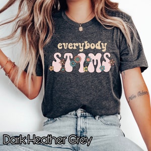 May include: Dark heather grey t-shirt with the text "everybody stims" in pink and yellow letters with flowers around the text.