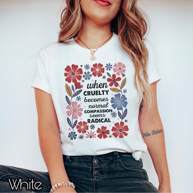 May include: White t-shirt with a floral design and the text "when CRUELTY becomes normal COMPASSION seems RADICAL". The flowers are red, pink, and blue. The shirt is a casual wear item.