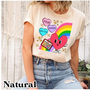 May include: A cream coloured t-shirt with a rainbow, a heart, and candy hearts that say "Your Words Matter".