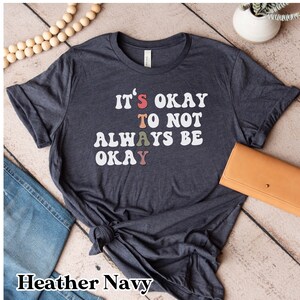 May include: Heather navy blue t-shirt with the text "It's okay to not always be okay" in white with colorful letters.