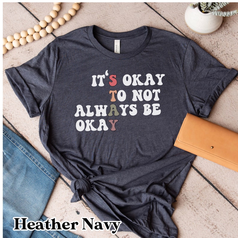 May include: Heather navy blue t-shirt with the text "It's okay to not always be okay" in white with colorful letters.