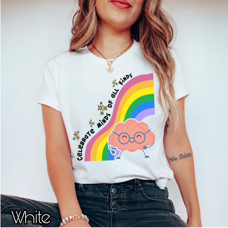 Pu&ograve; includere: Maglietta bianca con un arcobaleno e un cervello di cartone animato con gli occhiali. Il testo "Celebrate Minds of All Kinds" &egrave; scritto sull'arcobaleno.