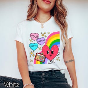 May include: White t-shirt featuring a rainbow, hearts, and a calculator. The hearts display the words "Your", "Words", and "Matter". The calculator has the word "WORD" on it.