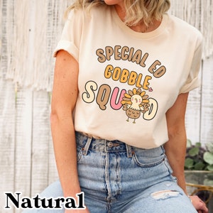 Peut inclure: Un t-shirt beige avec un motif graphique brun, jaune et rose qui dit "Special Ed Gobble Squad" avec une dinde de dessin anim&eacute; au milieu.
