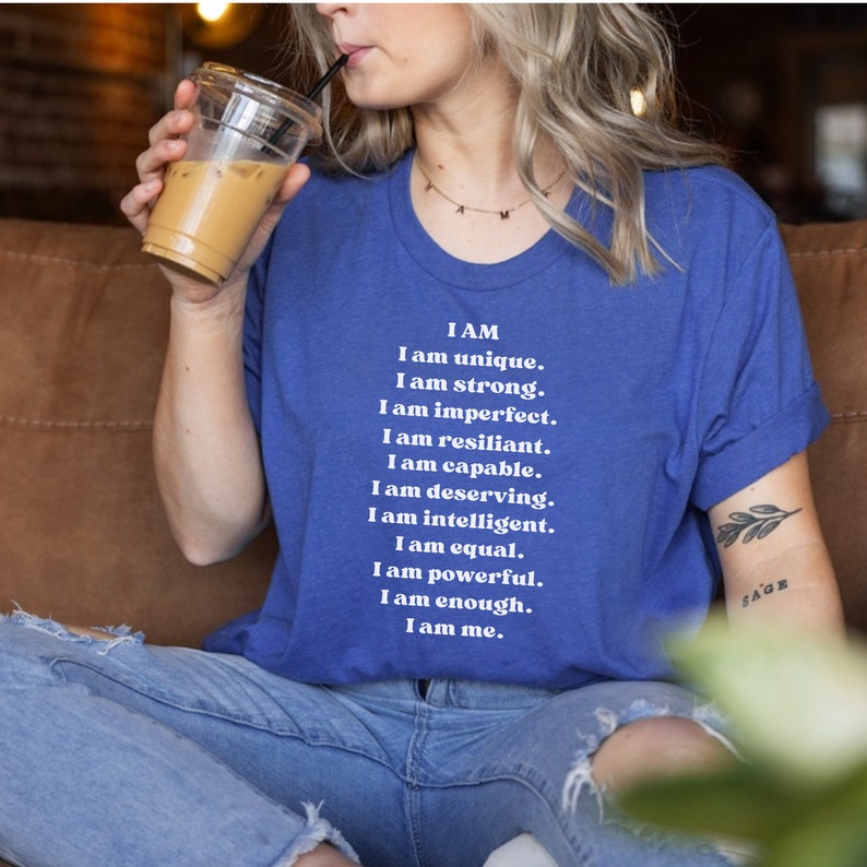 May include: A blue t-shirt with white text that reads "I AM I am unique. I am strong. I am imperfect. I am resilient. I am capable. I am deserving. I am intelligent. I am equal. I am powerful. I am enough. I am me."