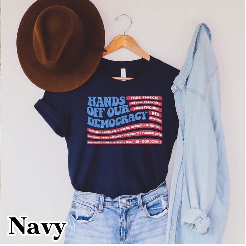 May include: Navy blue t-shirt with a red, white, and blue graphic that says "Hands Off Our Democracy". The graphic includes a list of issues such as free speech, federal programs, healthcare, and education.