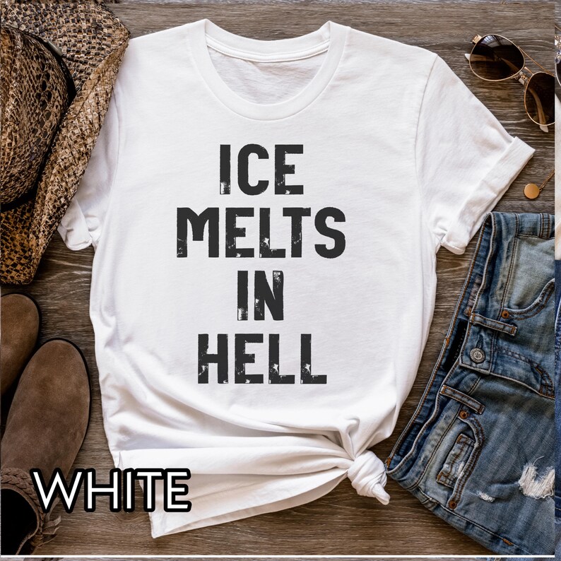 May include: White t-shirt with the text "ICE MELTS IN HELL" in black, distressed font. The word "WHITE" is at the bottom of the shirt. The shirt is knotted at the bottom. Sunglasses and a cowboy hat are in the background.