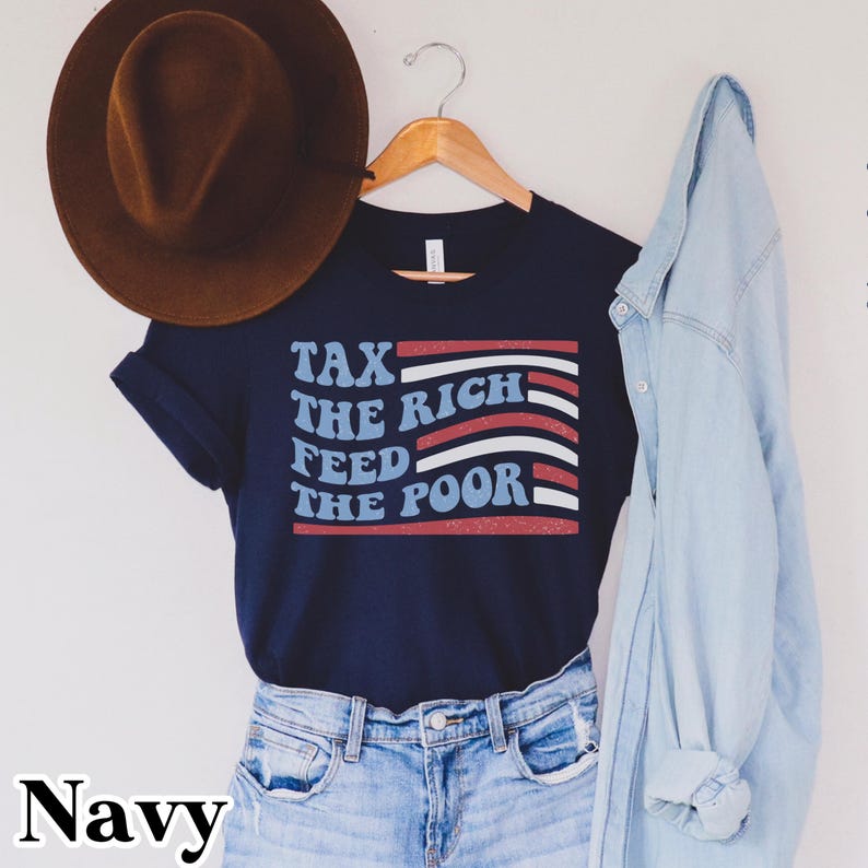 May include: Navy blue t-shirt with the text "TAX THE RICH FEED THE POOR" in white, red, and blue. A brown hat hangs above the shirt, and a light blue denim jacket is draped to the side. The word "Navy" is at the bottom.