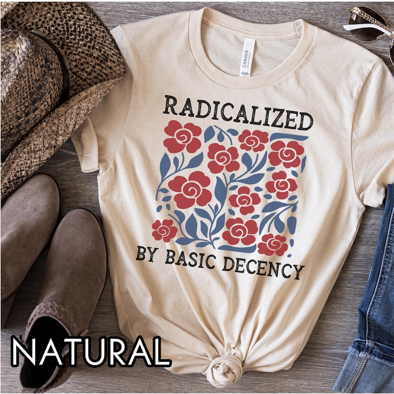 May include: A natural-colored t-shirt with the text "RADICALIZED BY BASIC DECENCY" in black. The shirt features a floral design with red roses and blue leaves. The shirt is knotted at the bottom.
