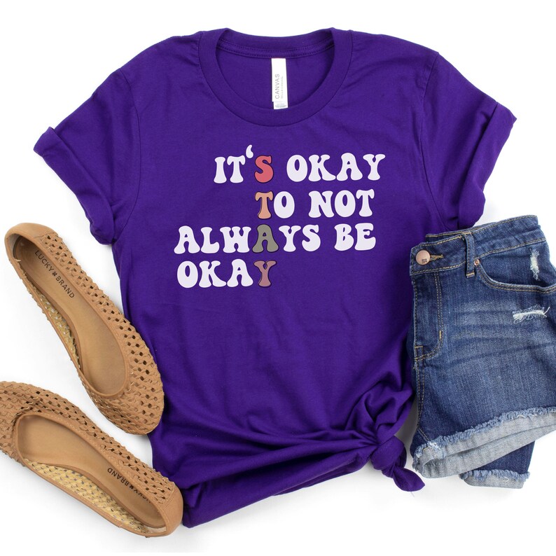 May include: Purple t-shirt with the text "It's okay to not always be okay" in rainbow colored letters.