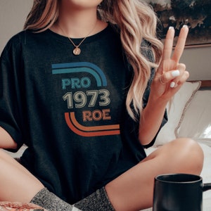 May include: A black t-shirt with a retro-style graphic that says "PRO 1973 ROE" in colorful text.