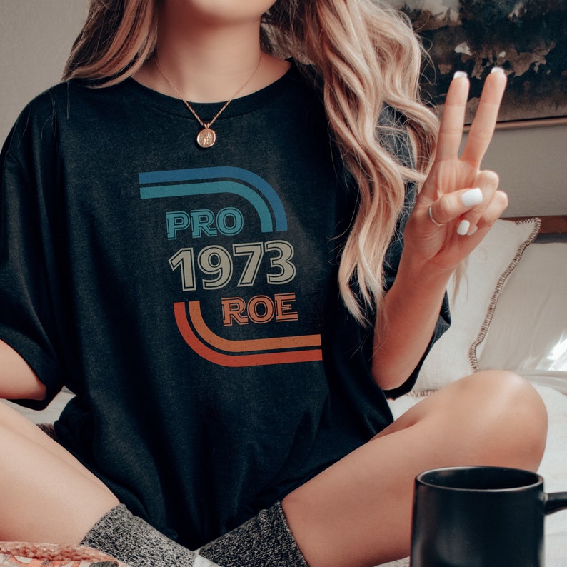 May include: A black t-shirt with a retro-style graphic that says "PRO 1973 ROE" in colorful text.