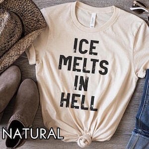 May include: A natural-colored t-shirt with the text "ICE MELTS IN HELL" in bold, black letters. The shirt is styled with a cowboy hat, sunglasses, and boots.