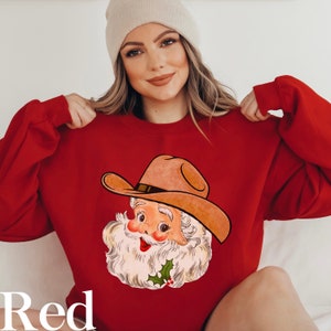 Puede incluir: Sudadera roja con una ilustraci&oacute;n de dibujos animados vintage de un Pap&aacute; Noel vaquero con un sombrero marr&oacute;n y una barba blanca.