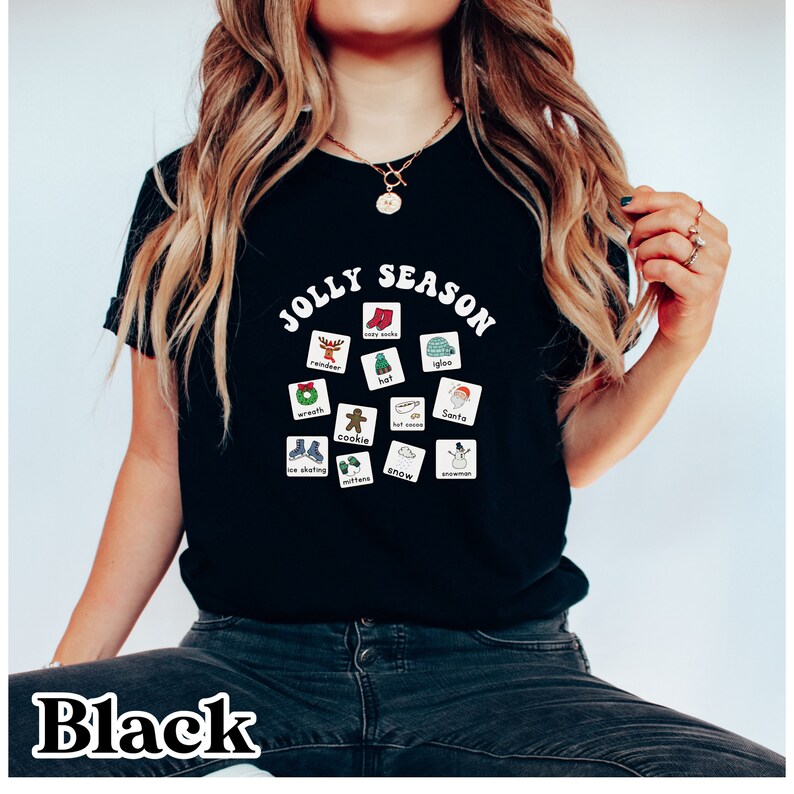K&ouml;nnte beinhalten: Schwarzes T-Shirt mit einer wei&szlig;en Grafik, auf der "Jolly Season" steht und ein Kreis mit weihnachtlichen Symbolen abgebildet ist. Die Symbole umfassen ein Rentier, einen Kranz, den Weihnachtsmann, einen Schneemann, einen Hut, F&auml;ustlinge, Schnee, hei&szlig;e Schokolade, einen Keks, Schlittschuhlaufen, kuschelige Socken und einen Iglu.